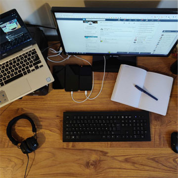 Bureau d'un collaborateur super connecté avec son ordinateur branché sur son ordinateur portable et son téléphone, un bloc note posé sur son bureau.